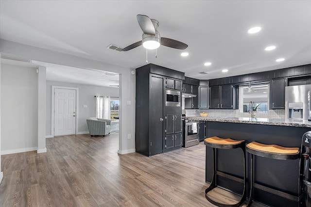 kitchen featuring a breakfast bar, hardwood / wood-style floors, stainless steel appliances, and light stone counters