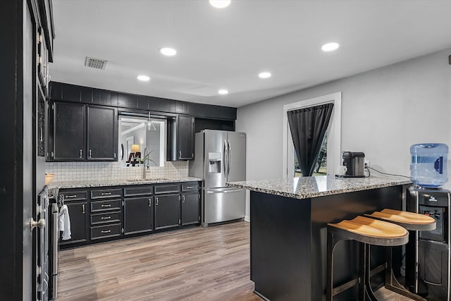 kitchen with kitchen peninsula, stainless steel fridge with ice dispenser, a breakfast bar, light wood-type flooring, and sink