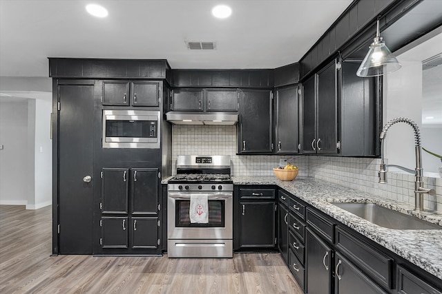 kitchen with decorative backsplash, hanging light fixtures, sink, light wood-type flooring, and appliances with stainless steel finishes