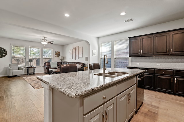 kitchen with light stone countertops, backsplash, ceiling fan, sink, and an island with sink