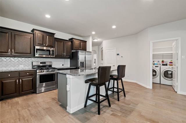 kitchen with a kitchen bar, separate washer and dryer, an island with sink, light stone counters, and stainless steel appliances