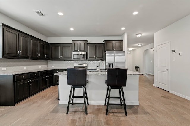 kitchen featuring light stone counters, a kitchen island with sink, appliances with stainless steel finishes, and a breakfast bar area