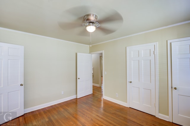 unfurnished bedroom featuring crown molding, two closets, hardwood / wood-style flooring, and ceiling fan