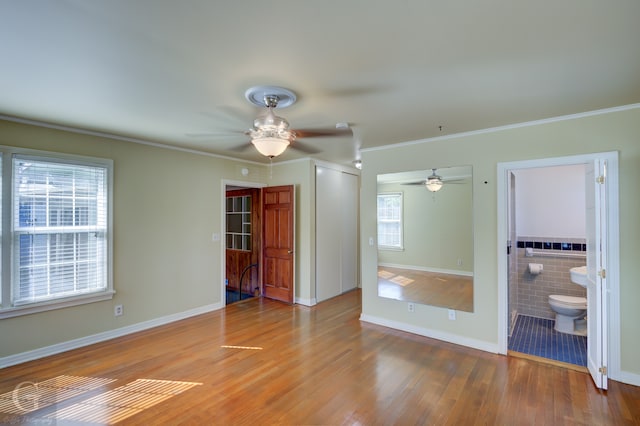 unfurnished bedroom with ceiling fan, tile walls, multiple windows, and hardwood / wood-style floors