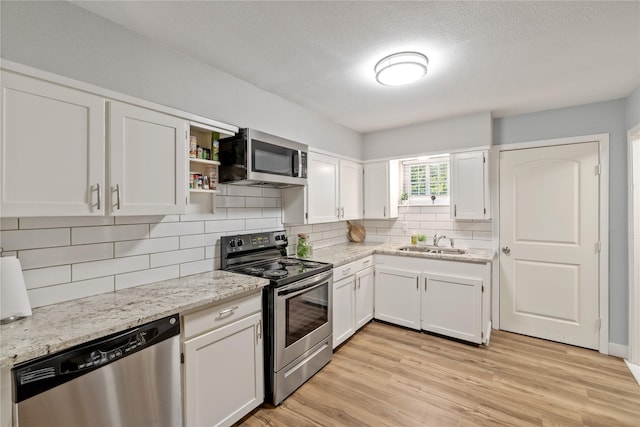 kitchen with appliances with stainless steel finishes, light wood-type flooring, white cabinetry, and sink