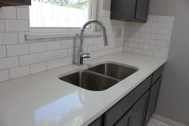 kitchen featuring gray cabinets, sink, light stone counters, and backsplash