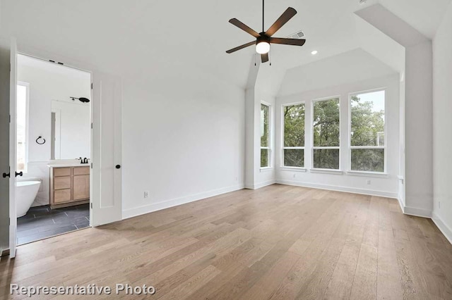 interior space featuring connected bathroom, ceiling fan, wood-type flooring, and vaulted ceiling