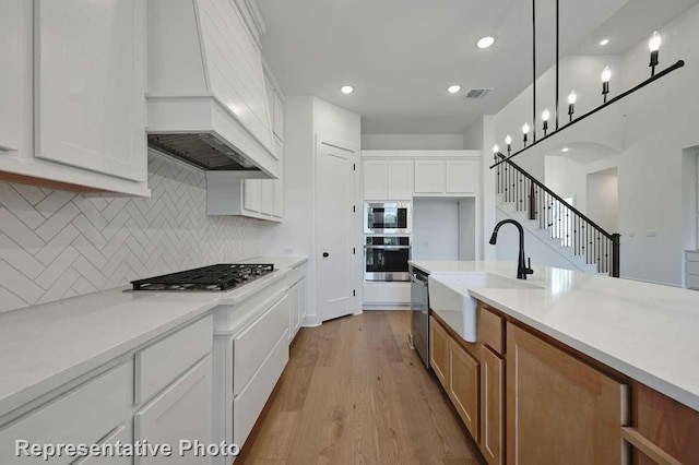 kitchen with light hardwood / wood-style flooring, sink, white cabinetry, premium range hood, and appliances with stainless steel finishes