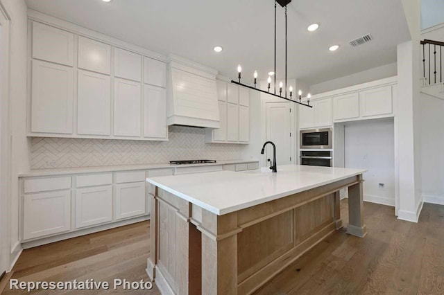 kitchen with pendant lighting, light hardwood / wood-style floors, an island with sink, and white cabinets