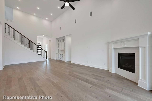 unfurnished living room with light hardwood / wood-style flooring, a high ceiling, and ceiling fan