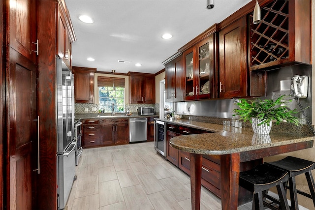 kitchen featuring a kitchen breakfast bar, backsplash, stainless steel appliances, sink, and dark stone countertops