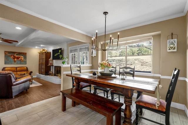 dining room featuring a brick fireplace, a healthy amount of sunlight, ceiling fan with notable chandelier, and ornamental molding