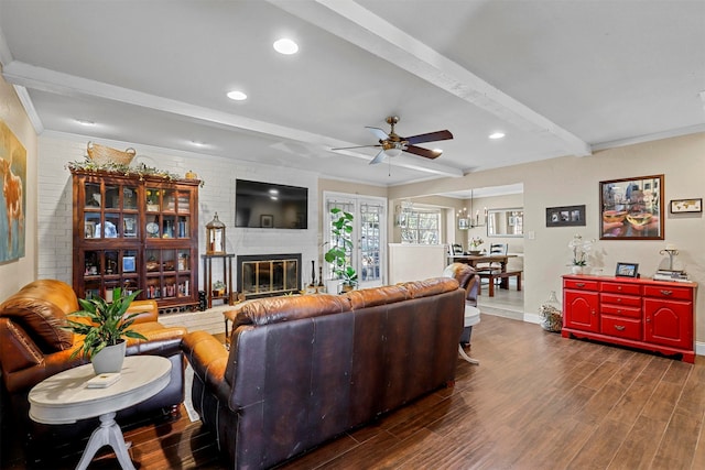 living room featuring a brick fireplace, brick wall, ceiling fan, dark wood-type flooring, and beamed ceiling