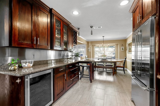 kitchen with stainless steel fridge, beverage cooler, crown molding, decorative light fixtures, and dark stone countertops