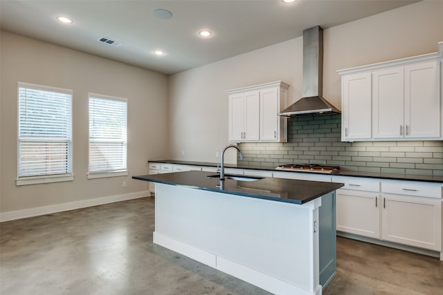 kitchen featuring white cabinets, wall chimney range hood, sink, an island with sink, and stainless steel gas cooktop