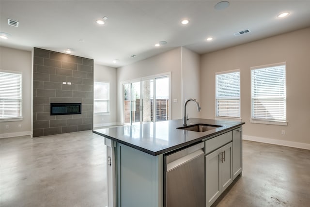 kitchen featuring a tiled fireplace, dishwasher, sink, and an island with sink