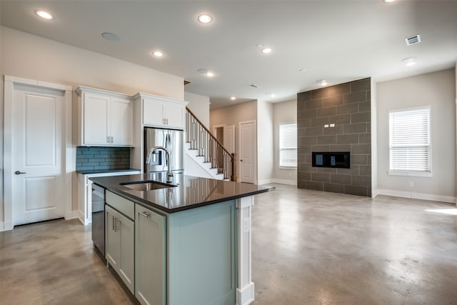 kitchen featuring a kitchen island with sink, a tile fireplace, sink, appliances with stainless steel finishes, and white cabinetry