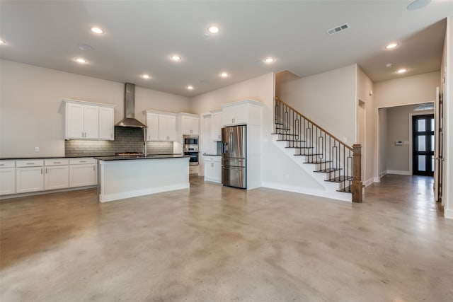 kitchen featuring decorative backsplash, appliances with stainless steel finishes, wall chimney exhaust hood, white cabinetry, and an island with sink