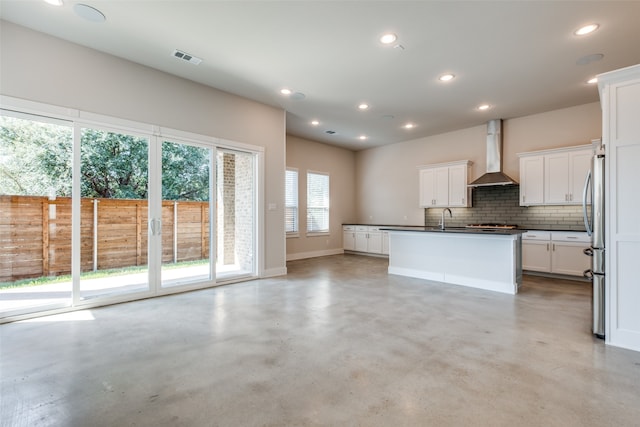 kitchen featuring backsplash, a kitchen island with sink, sink, wall chimney range hood, and white cabinetry