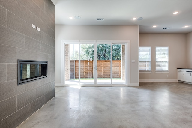 unfurnished living room featuring concrete flooring and a tiled fireplace