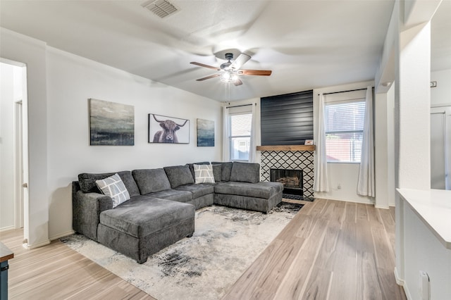 living room with ceiling fan, a fireplace, light wood-type flooring, and plenty of natural light