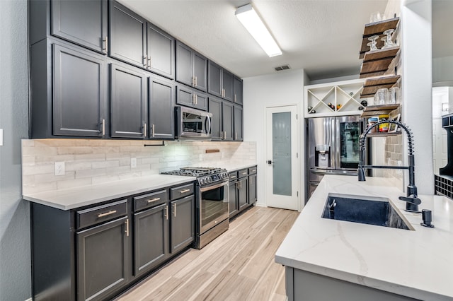 kitchen with decorative backsplash, light stone counters, appliances with stainless steel finishes, light hardwood / wood-style floors, and sink