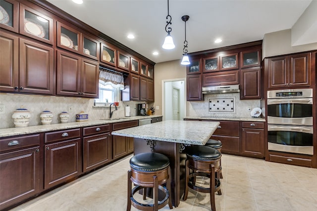 kitchen featuring decorative backsplash, a kitchen island, appliances with stainless steel finishes, a kitchen bar, and decorative light fixtures