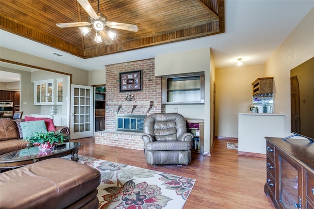 living room featuring light hardwood / wood-style floors, a tray ceiling, a fireplace, and ceiling fan