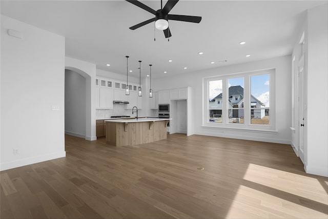 kitchen with dark wood-style floors, arched walkways, open floor plan, a sink, and an island with sink