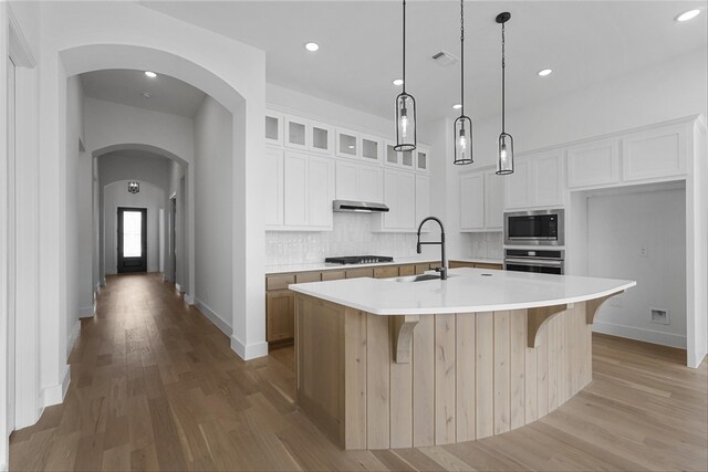 kitchen with a kitchen island with sink, light stone countertops, white cabinets, decorative light fixtures, and appliances with stainless steel finishes