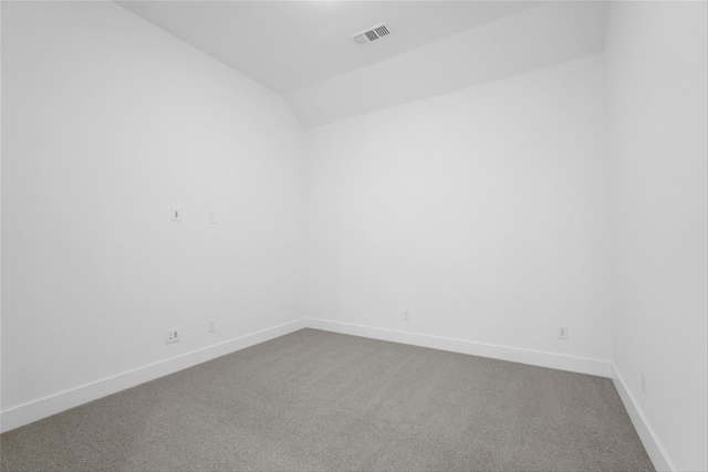 spare room featuring lofted ceiling, dark carpet, visible vents, and baseboards