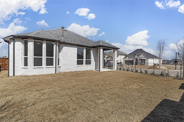 back of house with brick siding, a yard, a fenced backyard, and roof with shingles