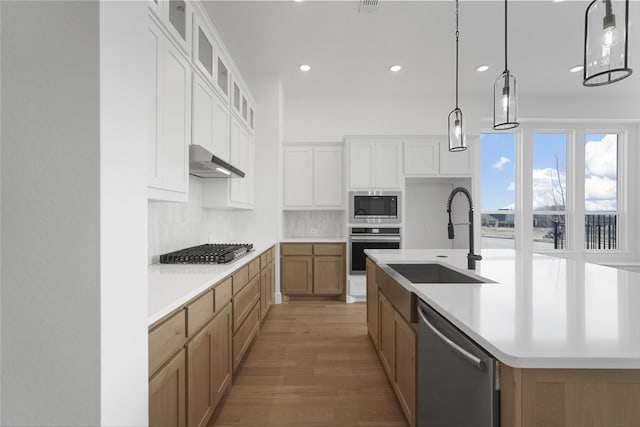 kitchen with a sink, light countertops, appliances with stainless steel finishes, wall chimney range hood, and backsplash