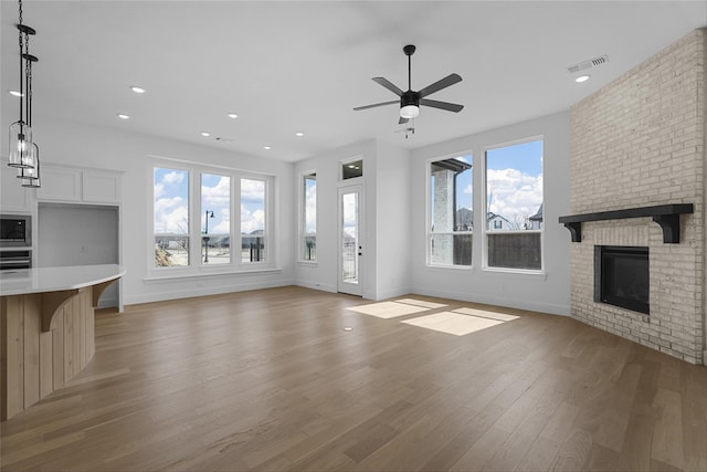 unfurnished living room featuring a brick fireplace, visible vents, a ceiling fan, light wood-style floors, and recessed lighting