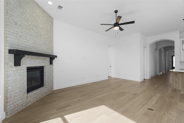 unfurnished living room with light wood-type flooring, visible vents, a fireplace, and ceiling fan