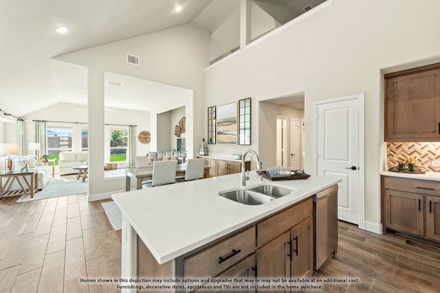 kitchen with dark wood-type flooring, an island with sink, sink, stainless steel dishwasher, and tasteful backsplash