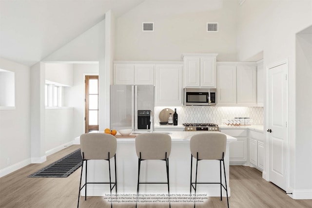 kitchen with a kitchen island, a kitchen bar, appliances with stainless steel finishes, tasteful backsplash, and high vaulted ceiling