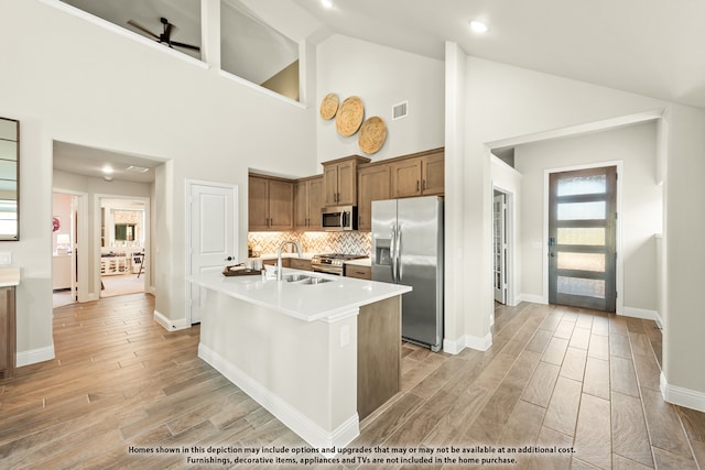 kitchen featuring sink, light wood-type flooring, stainless steel appliances, high vaulted ceiling, and a center island with sink