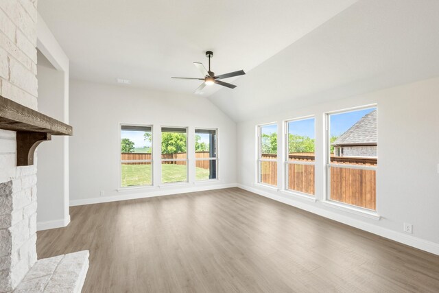 unfurnished living room with a stone fireplace, a ceiling fan, baseboards, wood finished floors, and lofted ceiling
