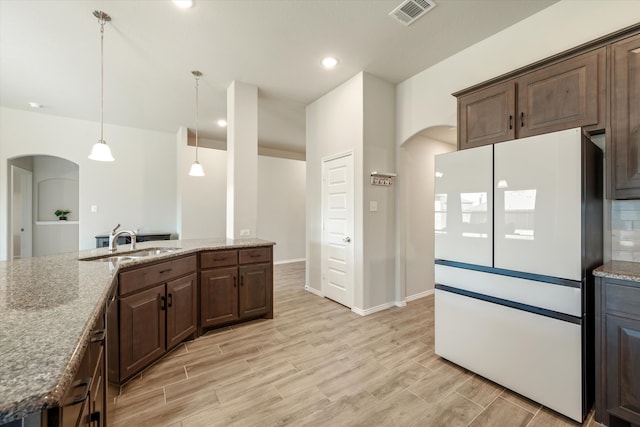 kitchen featuring pendant lighting, light hardwood / wood-style flooring, light stone countertops, dark brown cabinets, and white fridge