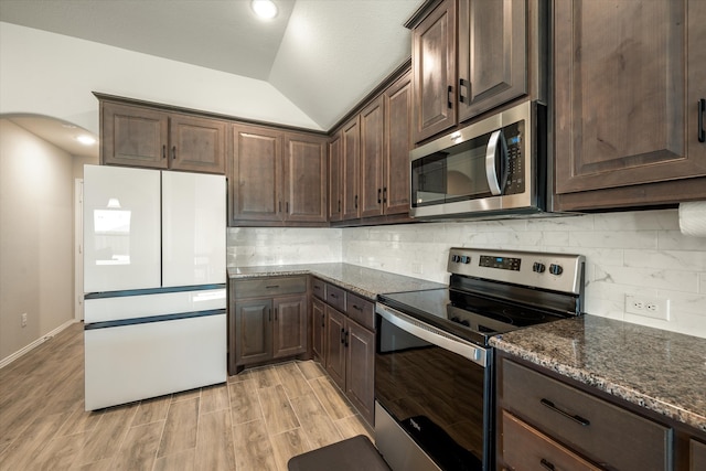 kitchen featuring decorative backsplash, appliances with stainless steel finishes, dark brown cabinetry, vaulted ceiling, and dark stone countertops