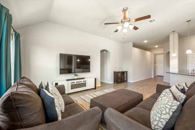 living room with ceiling fan, light hardwood / wood-style floors, and vaulted ceiling