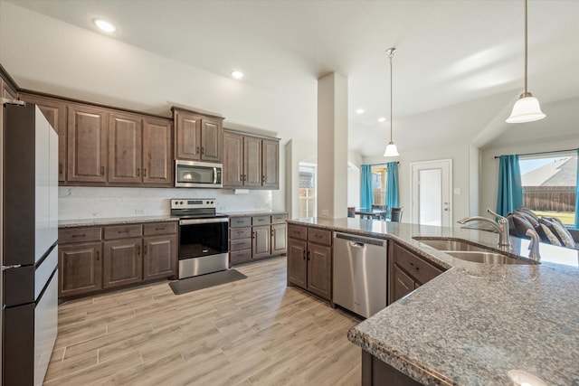 kitchen featuring sink, light wood-type flooring, decorative light fixtures, and appliances with stainless steel finishes