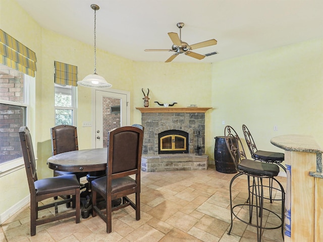 dining space featuring ceiling fan and a stone fireplace