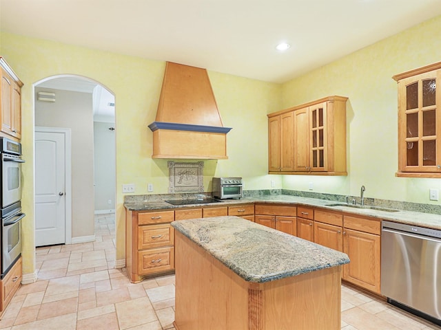 kitchen with sink, a center island, stainless steel appliances, light stone counters, and custom exhaust hood