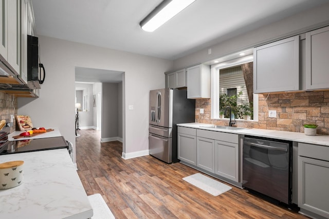 kitchen with hardwood / wood-style floors, backsplash, sink, gray cabinets, and stainless steel appliances