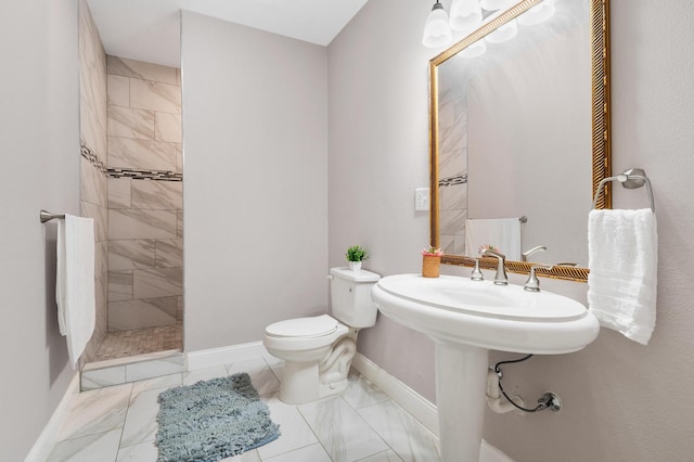 bathroom with toilet, marble finish floor, tiled shower, and baseboards