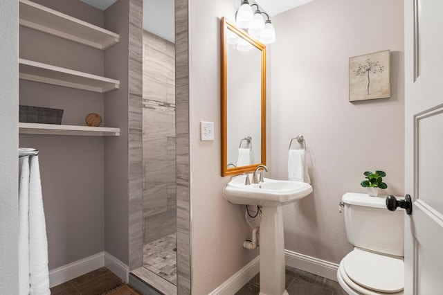 bathroom with a tile shower, toilet, and baseboards