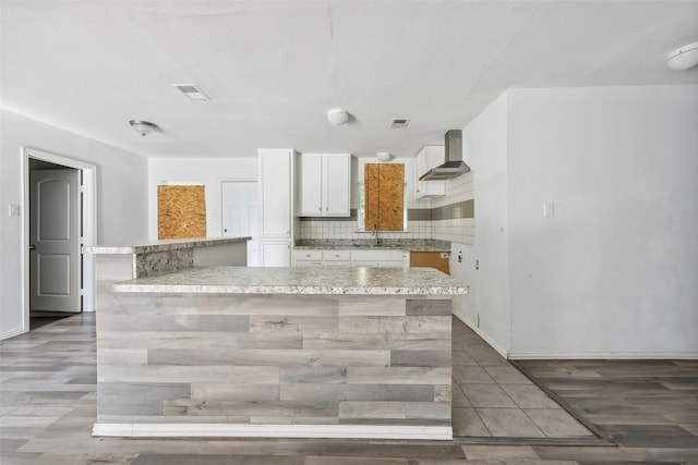 kitchen with wall chimney range hood, white cabinets, sink, light hardwood / wood-style floors, and a center island