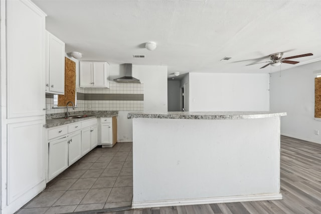 kitchen featuring wall chimney range hood, light hardwood / wood-style flooring, white cabinetry, and a center island